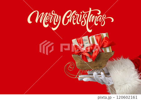 Merry Christmas, wooden sleigh figurine with gift boxes in Santa's hand with Merry Christmas inscription with space on red background with space for text 120602161