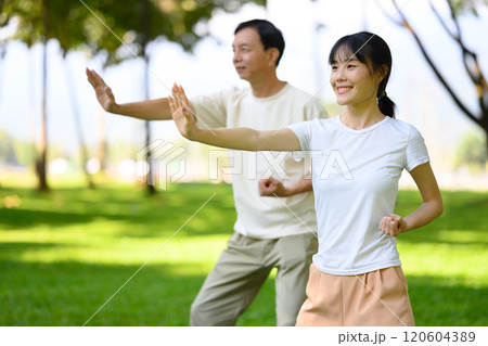 Pretty woman and middle aged man practicing Tai Chi together in scenic park. Mindfulness and health concept Pretty woman and middle aged man practicing Tai Chi together in scenic park. Mindfulness and health concept 120604389