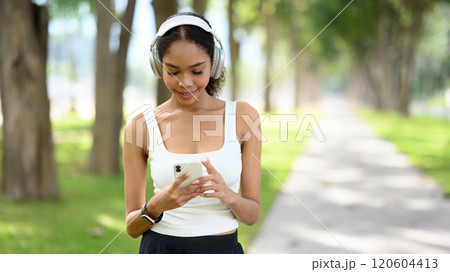 Curly haired active woman using mobile phone to track workout progress in the park Curly haired active woman using mobile phone to track workout progress in the park 120604413