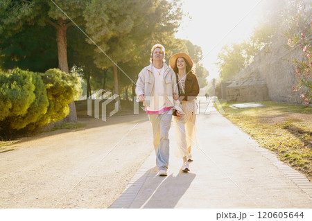 A couple strolls hand in hand through a sunlit park, sharing sweet, joyful moments A couple strolls hand in hand through a sunlit park, sharing sweet, joyful moments 120605644
