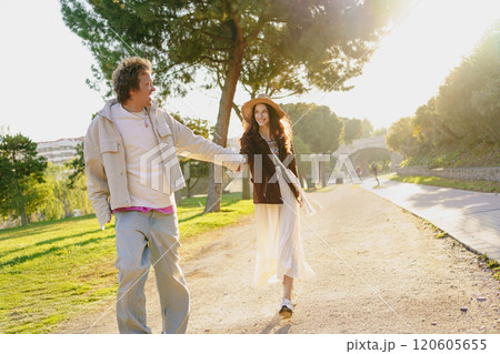 A Couple Walking Hand in Hand Together in a Bright Sunlit Park Full of Vibrant Fun and Love A Couple Walking Hand in Hand Together in a Bright Sunlit Park Full of Vibrant Fun and Love 120605655