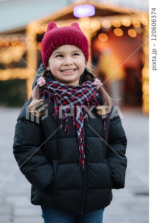 Portrait of adorable little girl standing in front of Christmas lights in old town. Background of bokeh  120606374
