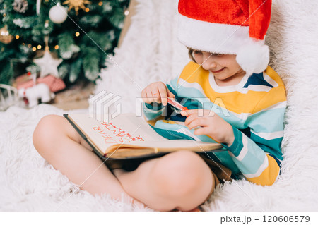 Smiling Kid boy in red Santa hat sit on couch and writing the letter to dear Santa at home. Child wish list. Dreams of a Christmas gifts. Merry Christmas and Happy new year. Smiling Kid boy in red Santa hat sit on couch and writing the letter to dear Santa at home. Child wish list. Dreams of a Christmas gifts. Merry Christmas and Happy new year. 120606579