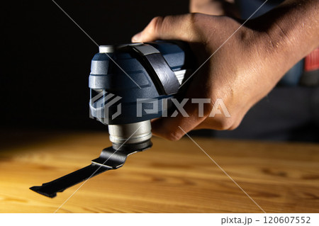 A person holds a versatile oscillating Multi Cutter tool, ready to tackle detailed woodworking or renovation tasks A person holds a versatile oscillating Multi Cutter tool, ready to tackle detailed woodworking or renovation tasks 120607552