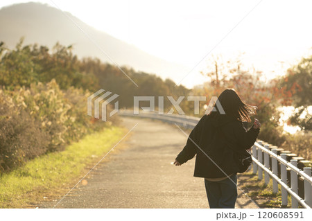 夕方の秋の景色の道を楽しそうに歩く女性の後ろ姿 120608591