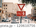 A bustling city street with a bicycle and pedestrian sign, surrounded by buildings and trees. Vehicles and pedestrians share the road in this urban setting 120610756