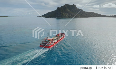 Aerial drone view red cargo ship navigate turquoise waters near volcanic Maupiti island, French Polynesia, leaving a white trail behind it on a sunny day. Delivery bulk carrier to exotic remote places Aerial drone view red cargo ship navigate turquoise waters near volcanic Maupiti island, French Polynesia, leaving a white trail behind it on a sunny day. Delivery bulk carrier to exotic remote places 120610781
