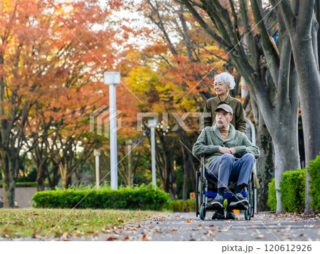 歩道を歩く車椅子に乗った男性と介助する女性のシニアカップル 120612926