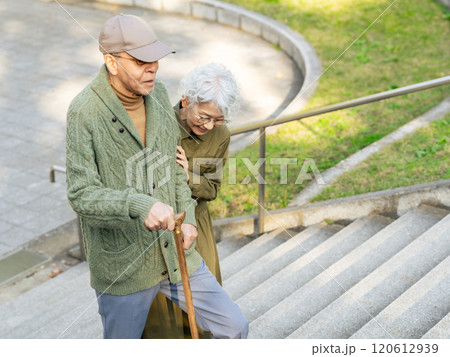 杖をついて階段を登る男性とサポートする女性のシニアカップル 杖をついて階段を登る男性とサポートする女性のシニアカップル 120612939