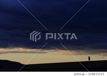 どんよりとした雲が広がる夕方の堤防を歩く人 120613221