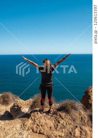Girl standing on the edge of a cliff with outstretched arms 120613397