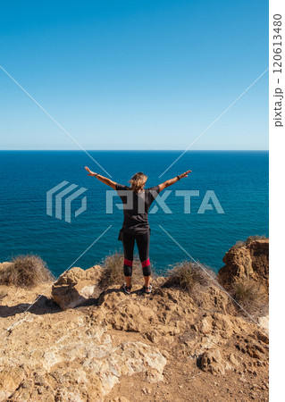 Girl standing on the edge of a cliff with outstretched arms 120613480