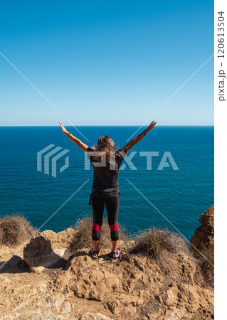 Girl standing on the edge of a cliff with outstretched arms 120613504