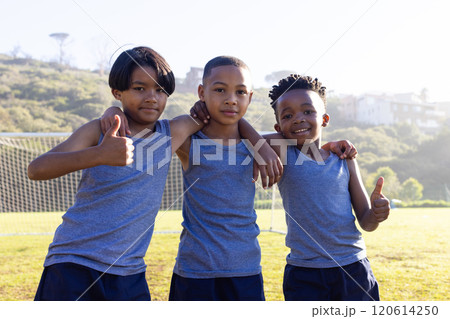 Outdoors, standing together on soccer field, three multiracial boys in uniforms giving thumbs up 120614250