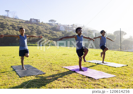 Practicing yoga, three multiracial boys balancing on mats outdoors at school 120614256