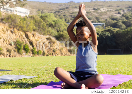 Practicing yoga, african american boy sitting on mat outdoors, meditating in peaceful setting Practicing yoga, african american boy sitting on mat outdoors, meditating in peaceful setting 120614258
