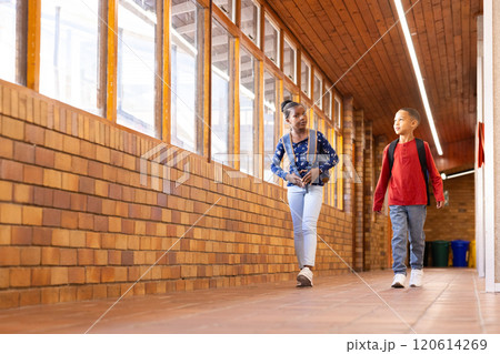 Walking in school hallway, two multiracial boy and girl with backpacks talking and smiling Walking in school hallway, two multiracial boy and girl with backpacks talking and smiling 120614269