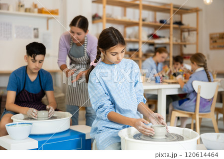 Children working at potter's wheel with teacher in art studio Children working at potter's wheel with teacher in art studio 120614464