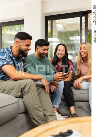 diverse friends sitting on couch, laughing and looking at smartphone together diverse friends sitting on couch, laughing and looking at smartphone together 120614569