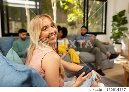 Smiling woman holding smartphone, sitting with friends in living room, socializing 120614587