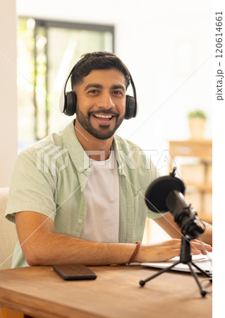 Smiling man recording podcast with microphone and headphones at home office 120614661
