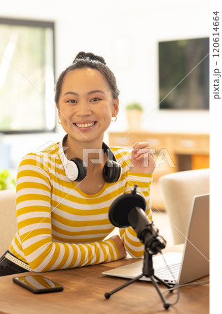 Smiling woman with headphones recording podcast using laptop and microphone 120614664