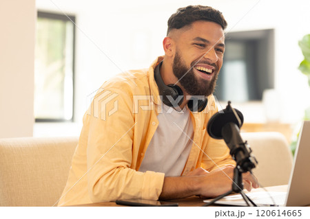 Smiling man with headphones recording podcast using microphone and laptop 120614665