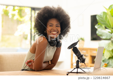 Smiling african american woman with headphones and microphone recording podcast at home office 120614667