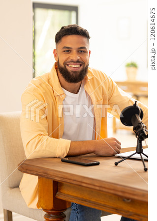 Smiling man sitting at table with microphone and smartphone, ready for podcast 120614675