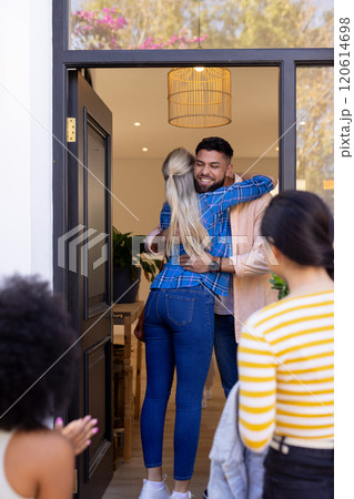 Welcoming friends, man hugging woman at front door, others arriving 120614698