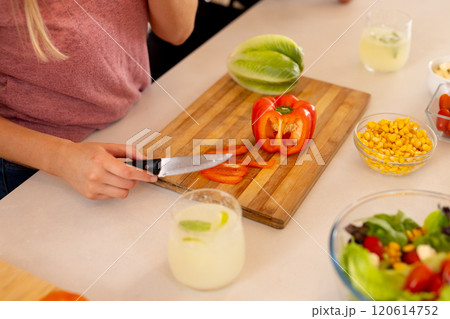 Slicing red bell pepper on cutting board, person preparing fresh salad ingredients 120614752