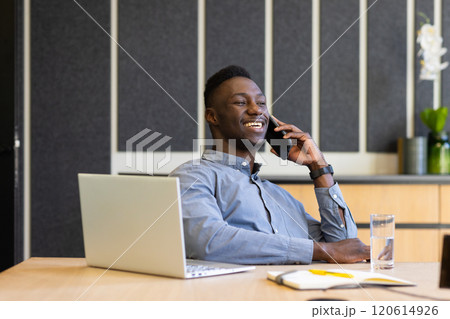Talking on smartphone, man smiling and working on laptop at office desk Talking on smartphone, man smiling and working on laptop at office desk 120614926