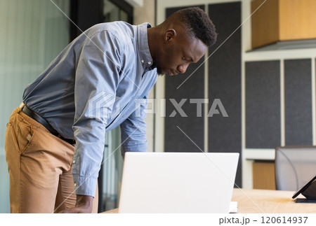 Working in office, man leaning over desk and focusing on laptop screen 120614937
