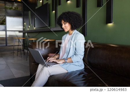 Working on laptop, businesswoman sitting on couch in modern office space 120614983