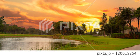 A glowing sunset over a tranquil golf course with a serene pond, vibrant skies, and lush greenery, offering a peaceful retreat. 120615254