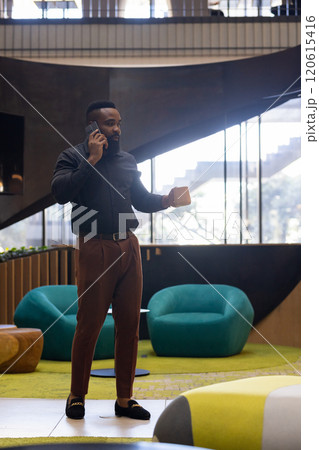 Talking on smartphone, African american man holding coffee cup in modern office environment Talking on smartphone, African american man holding coffee cup in modern office environment 120615416