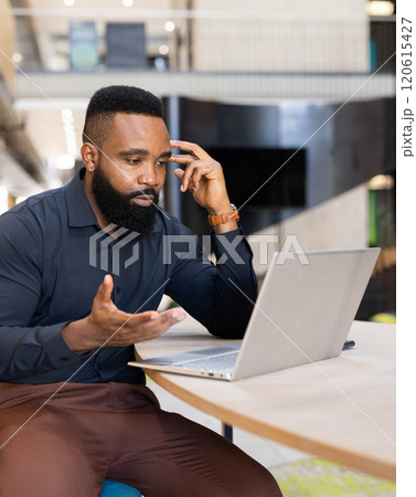 Using laptop and talking on phone, man working in modern office setting Using laptop and talking on phone, man working in modern office setting 120615427