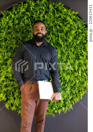 Holding clipboard, African American businessman standing confidently in front of green wall 120615431