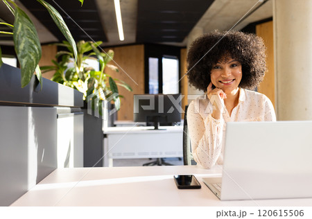Smiling woman working on laptop with smartphone on desk in modern office, copy space 120615506