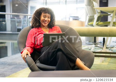 Smiling woman sitting in chair using tablet in modern office environment 120615534