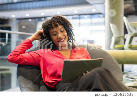 Smiling businesswoman using tablet while sitting in modern office lounge area 120615535
