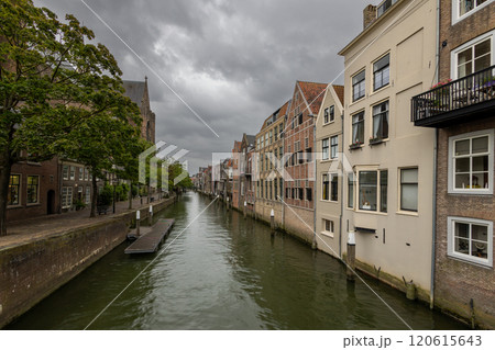 A picturesque canal scene with historic European-style buildings, a cobblestone pathway, and trees under an overcast sky, capturing the charm and tranquility of the location. Dordrecht landscape. 120615643