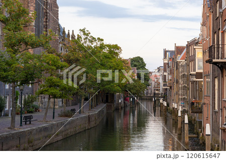 A picturesque canal scene with historic European-style buildings, a cobblestone pathway, and trees under an overcast sky, capturing the charm and tranquility of the location. Dordrecht landscape. 120615647