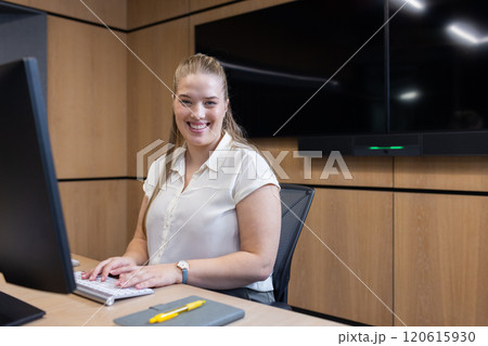 Smiling woman working on computer at office desk with notepad and pen Smiling woman working on computer at office desk with notepad and pen 120615930