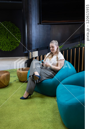 Using smartphone, businesswoman sitting on bean bag chair in modern office 120615955