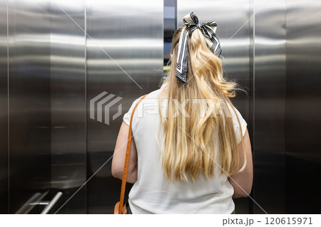 Entering elevator, woman with long blonde hair and striped bow in office building Entering elevator, woman with long blonde hair and striped bow in office building 120615971