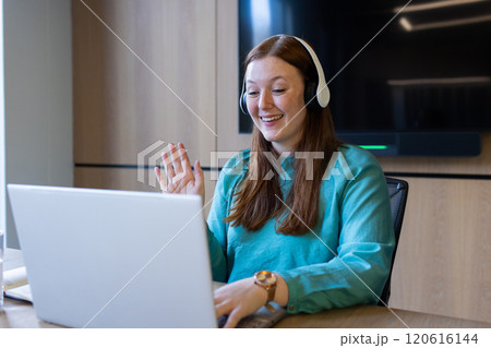 Waving and smiling, woman using laptop and wearing headphones in office 120616144