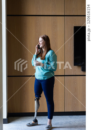 Talking on smartphone, woman with prosthetic leg standing in modern office 120616154
