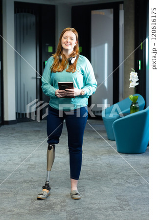 Woman with prosthetic leg holding tablet and smiling in modern office setting 120616175