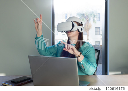 At office, Using VR headset, woman interacting with virtual environment while working on laptop 120616176